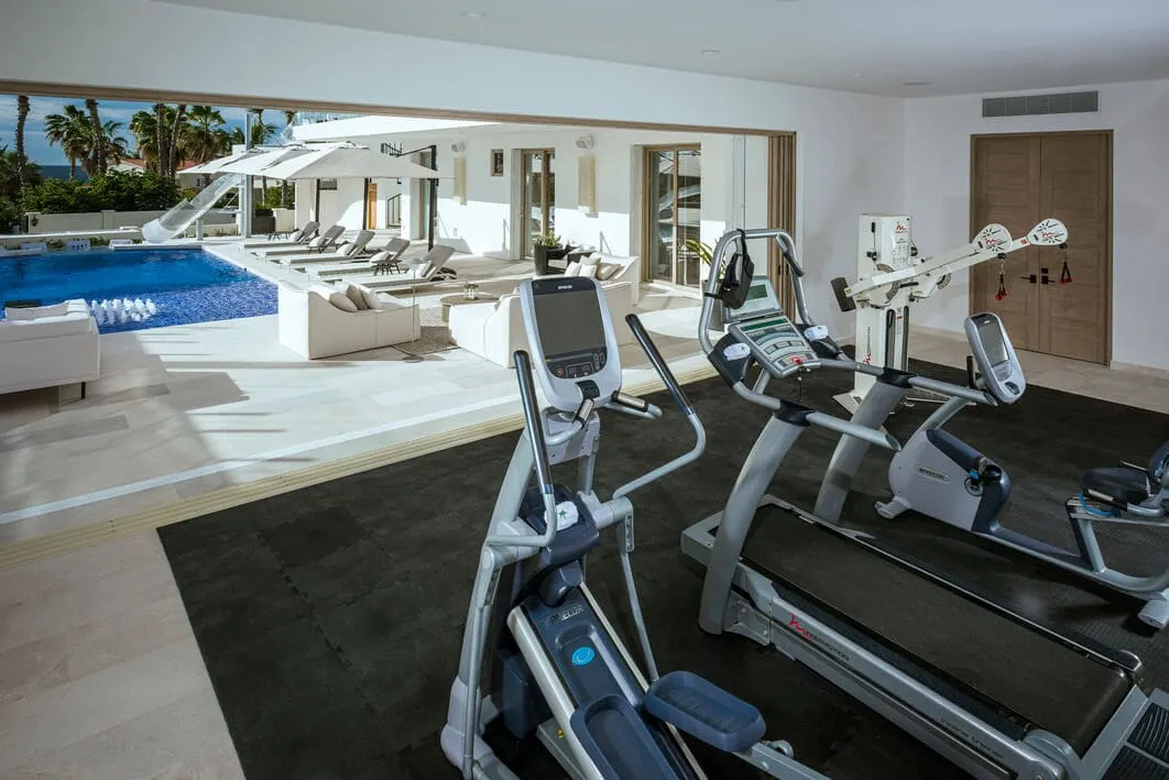 Home gym with treadmill and elliptical overlooking the pool and lounge terrace at Casa Aqua Blanca