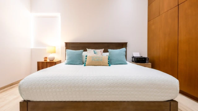 cama confortable hospedaje dunas condo Double bed with a textured white quilt and decorative cushions in blue and neutral tones