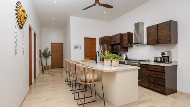 cocina equipada dunas condo Open kitchen with an island, rope stools, dark cabinets, and a sun wall decor.