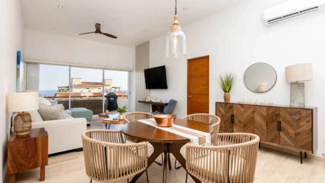comedor vista mar dunas condo Round wooden dining table with rope chairs, a credenza, and a partial ocean view from the balcony.