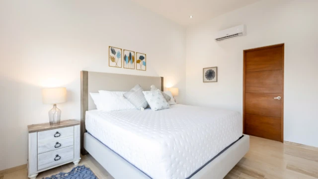 cuarto amplio decoracion hospedaje dunas condo Vacation bedroom with a bed, rustic nightstand, botanical wall decor, and wooden finishes.