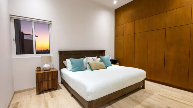 recamara atardecer dunas condo Bedroom with a large bed, wooden closet, and a window with a colorful sunset view.