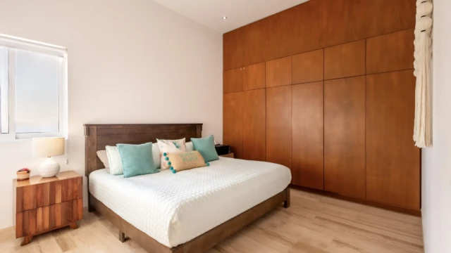 recamara principal closet dunas condo Bright bedroom with a large bed, turquoise cushions, and a wall-to-wall wooden closet.