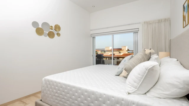 recamara vista balcon dunas condo Large bed with white linens next to a sliding glass door opening to a private balcony.