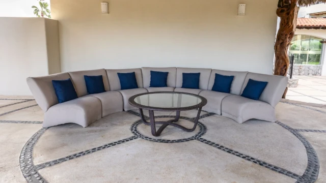 sala exterior palapa dunas condo Outdoor living room with a curved sofa and a glass table under a rustic palapa.